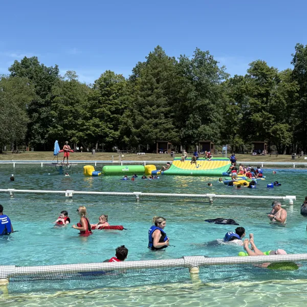 People swimming in a pool with inflatable obstacle course, trees in background.